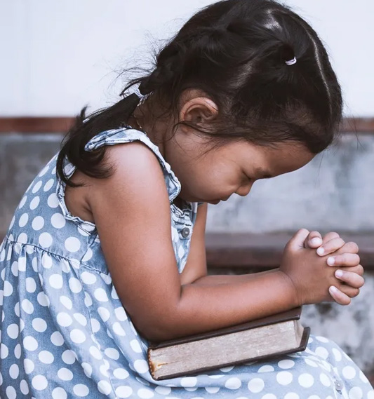 A little girl sitting down with her hands clasped in front of her knees.